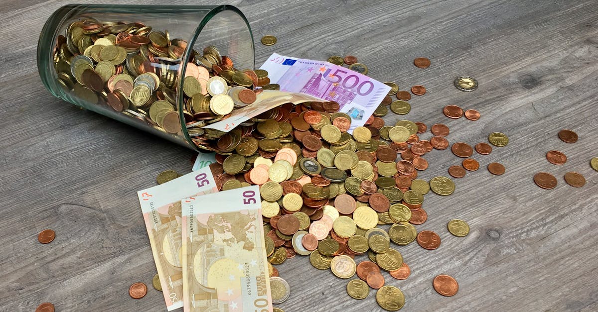 A glass jar with euro coins and banknotes spilled on a wooden surface, representing finance and savings.